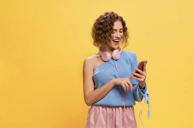 Pembe kulaklıklı bir model telefonu tutuyor, gülümsüyor..