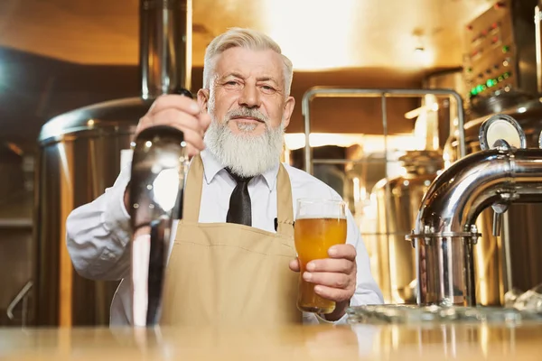 Anciano barman de pie en el mostrador del bar con vaso de cerveza . — Foto de Stock