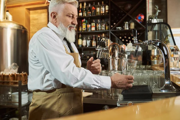 Barman de pie en el mostrador del bar vertiendo cerveza en vidrio . — Foto de Stock