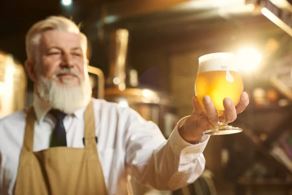 Cervejeiro positivo segurando vidro de cerveja com espuma . — Fotografia de Stock