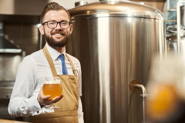 Cervejeiro barbudo segurando vidro de cerveja fria com espuma . — Fotografia de Stock