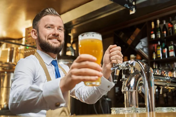 Barman guapo sosteniendo vaso de cerveza lager frío . — Foto de Stock