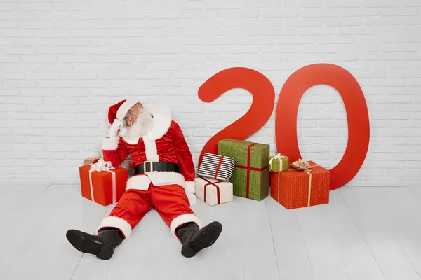 Zmęczony Święty Mikołaj siedzi na podłodze w pobliżu czerwonego pudełka prezentów — Zdjęcie stockowe