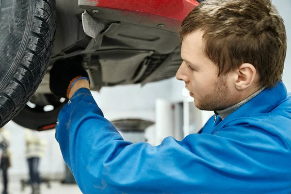 Competent mechanic in blue uniform examining car suspension