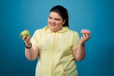 Tombul kız yeşil elma ya da lezzetli donut yemeyi seçiyor.