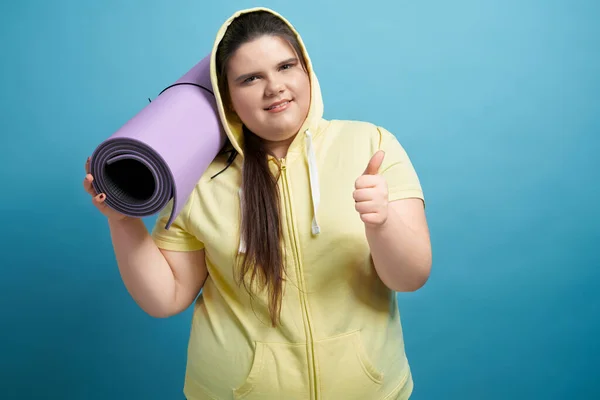 Junge übergroße Mädchen halten Matte und zeigen Zeichen super — Stockfoto