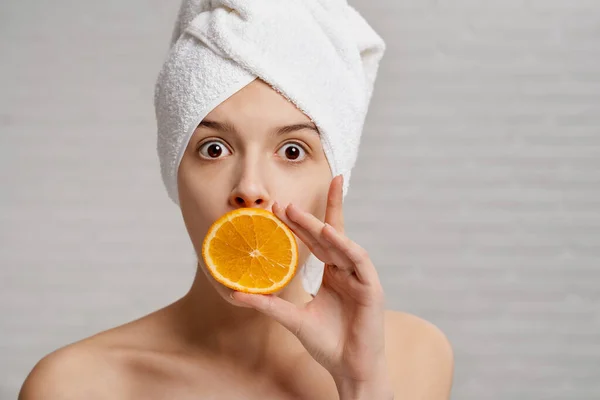 Woman with wide open eyes holding slice of orange.