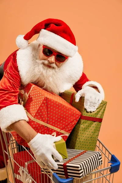 Idős férfi Mikulás jelmezben ajándékdobozokkal a bevásárlókosárban — Stock Fotó