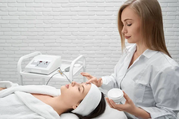 Médico aplicar crema en la cara de la mujer joven . — Foto de Stock