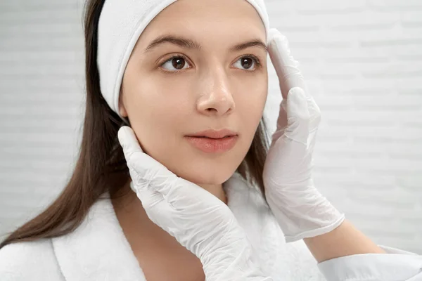 Cosmetólogo en guantes blancos inspeccionando la cara del paciente . — Foto de Stock