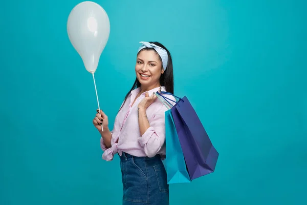 Beautiful woman keeping paper bags and balloon and posing