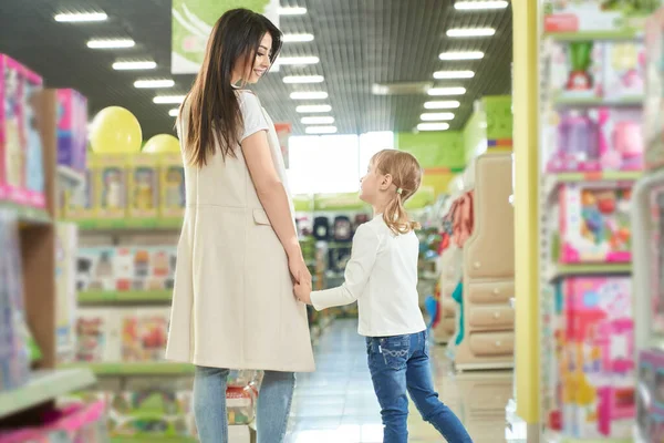 Ευτυχισμένη μητέρα και κορίτσι με τα πόδια στο εμπορικό κέντρο, κατάστημα παιχνιδιών. — Φωτογραφία Αρχείου