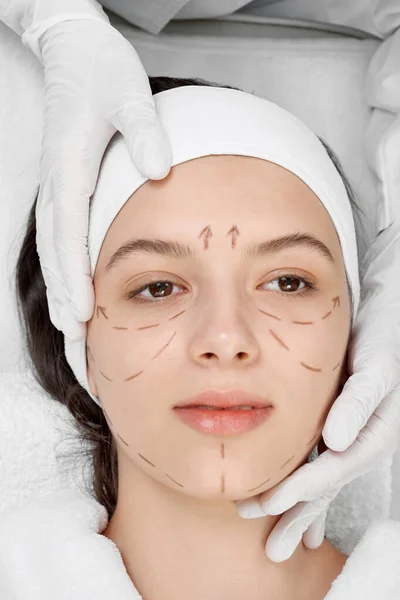 Woman with black surgical lines in cosmetology cabinet.