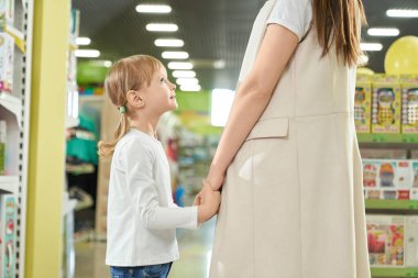 Neşeli kız. Annesinin elini dükkanda tutuyor ve gülümsüyor.