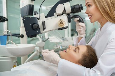 Stomatolog mikroskop kullanarak hastanın dişlerini inceliyor..