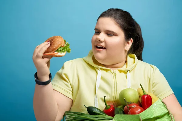 Klobige Frau versucht, Burger statt gesundem Essen zu essen — Stockfoto