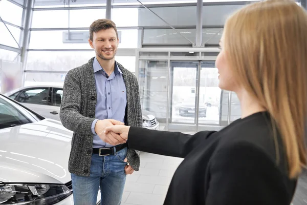 Sourire client masculin serrant la main au vendeur dans la salle d'exposition de la voiture — Photo