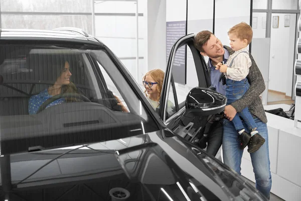 View from side of happy family looking at car in auto salon