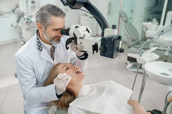 Medico guardando attraverso il microscopio dentale ai denti della donna . — Foto Stock