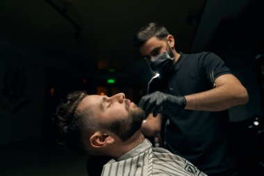 Salonda oturup sakal tıraşı olan bir adamın yan görüntüsü.