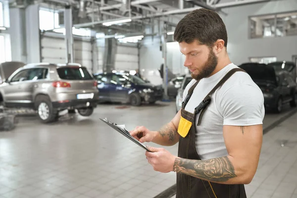 Muscular mechanic in coveralls reading from folder. — Stockfoto