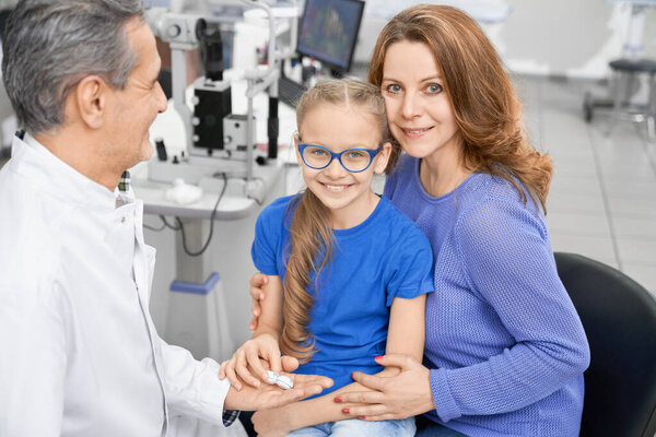Mother sitting with little daughter and checking eyesight