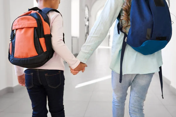 School girls with colorful backpacks holding by hands.