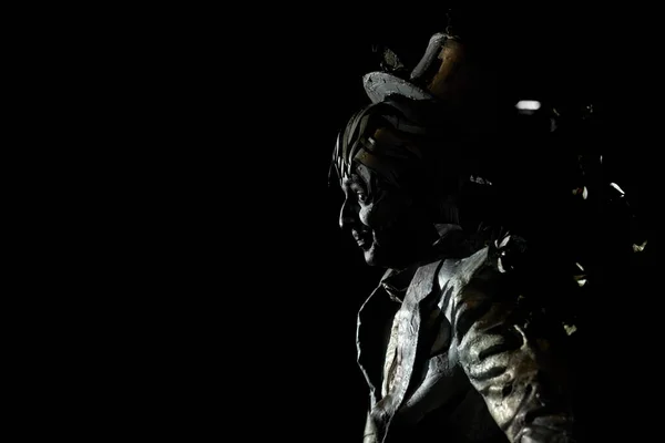 Side view of mime imitating statue on black background