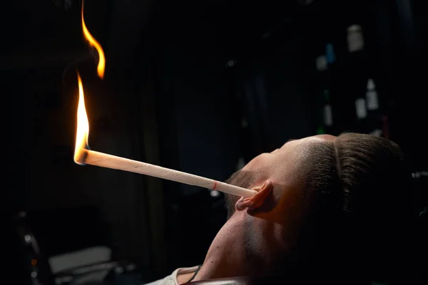 Close up of mans head with burning stick in ear at salon — Stock Photo, Image