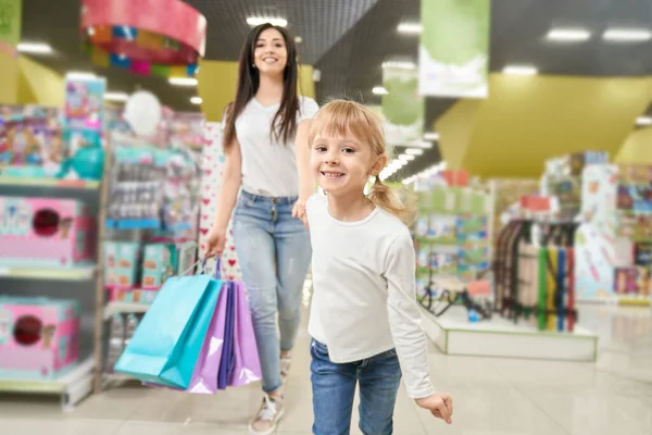 Дівчина тримає руку мами і бігає вперед в магазині іграшок — стокове фото