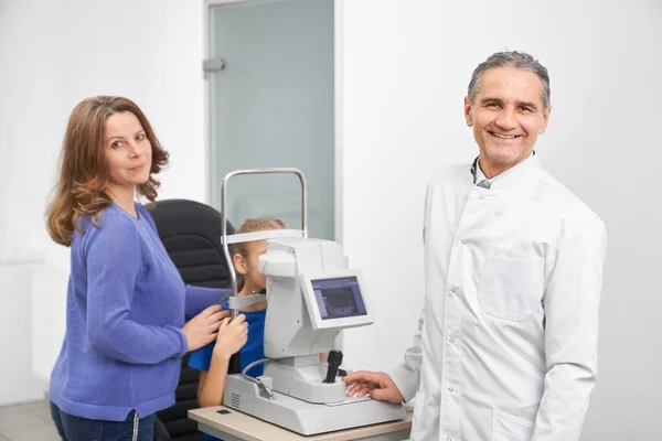 Male oculist and mother posing while checking sight of girl — Stock Photo, Image