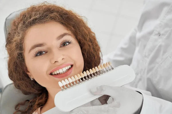 Mulher sorrindo enquanto dentista masculino mantendo a faixa de cores dos dentes — Fotografia de Stock