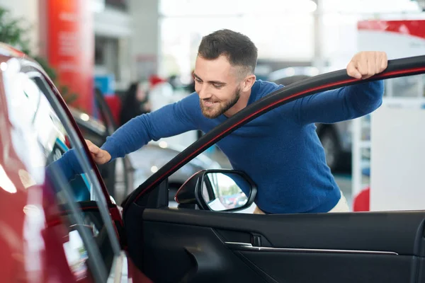 Pria berjanggut tersenyum memeriksa mobil di dealer. — Stok Foto
