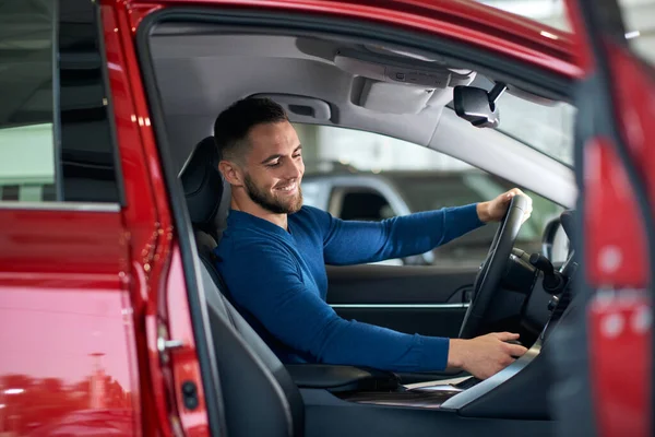 Happy male customer in car in dealership.