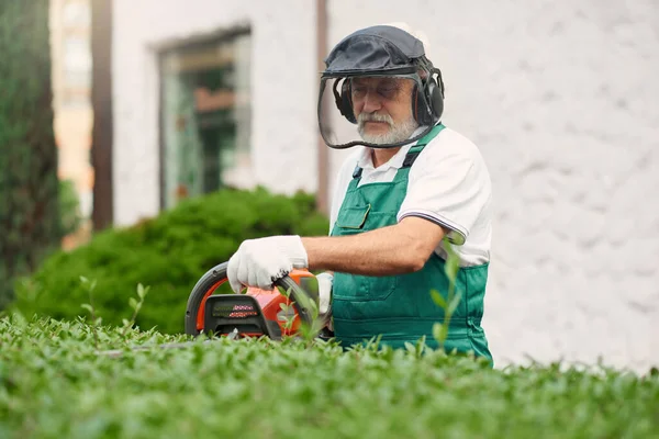 Muž nosí ochranu ucha a obličeje pomocí ořezávacího stroje. — Stock fotografie