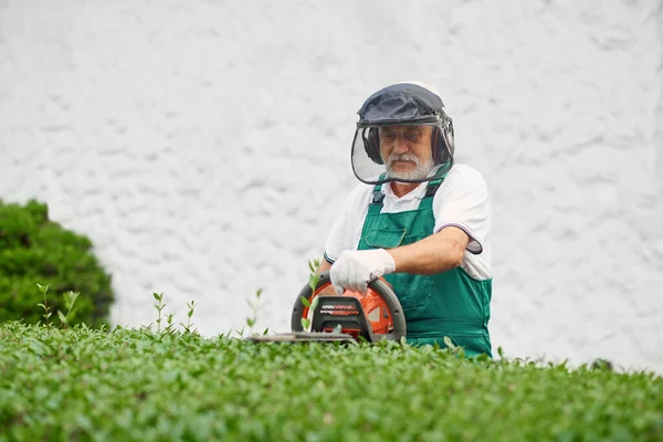 Muž nosí ochranu ucha a obličeje pomocí ořezávacího stroje. — Stock fotografie