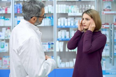 Woman with headache asking pharmacist for pills. clipart