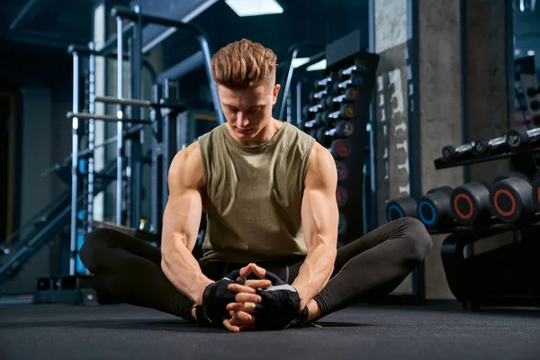 Bodybuilder gör fjäril sträcka på golvet i gymmet. — Stockfoto