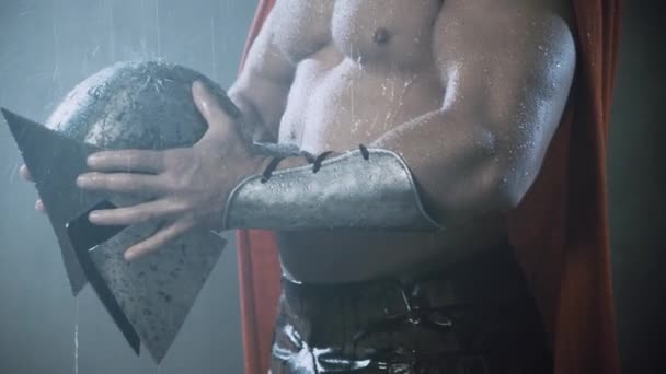 Wet spartan holding helmet under rain. — Stock Video