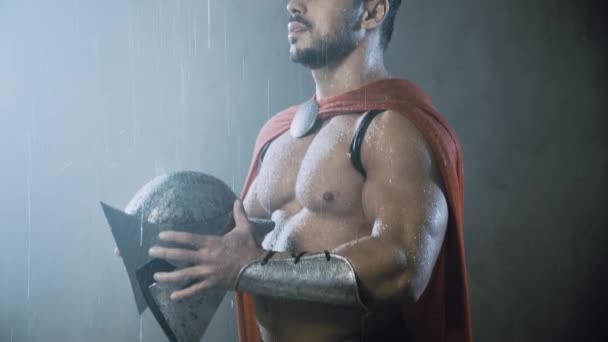 Wet spartan holding helmet under rain. — Stock Video