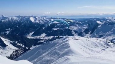 Karlı dağların üzerindeki paraşüt uçaklarında uçan turistler.