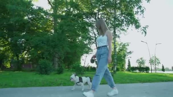 Улыбающаяся женщина гуляет с французским бульдогом в парке. — стоковое видео