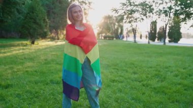 Vücudunun etrafında gökkuşağı bayrağı taşıyan gülümseyen kadın.