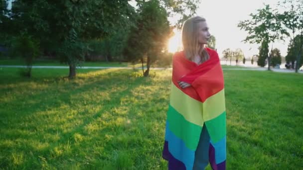 Mujer sonriente sosteniendo la bandera del arco iris alrededor del cuerpo . — Vídeo de stock