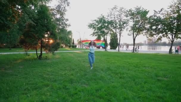 Mujer corriendo con bandera de arco iris, mostrando tolerancia. — Vídeos de Stock