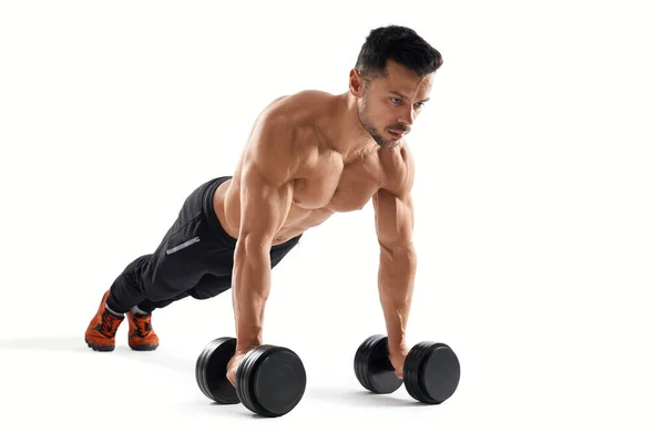 Hombre musculoso haciendo flexiones usando pesas . — Foto de Stock