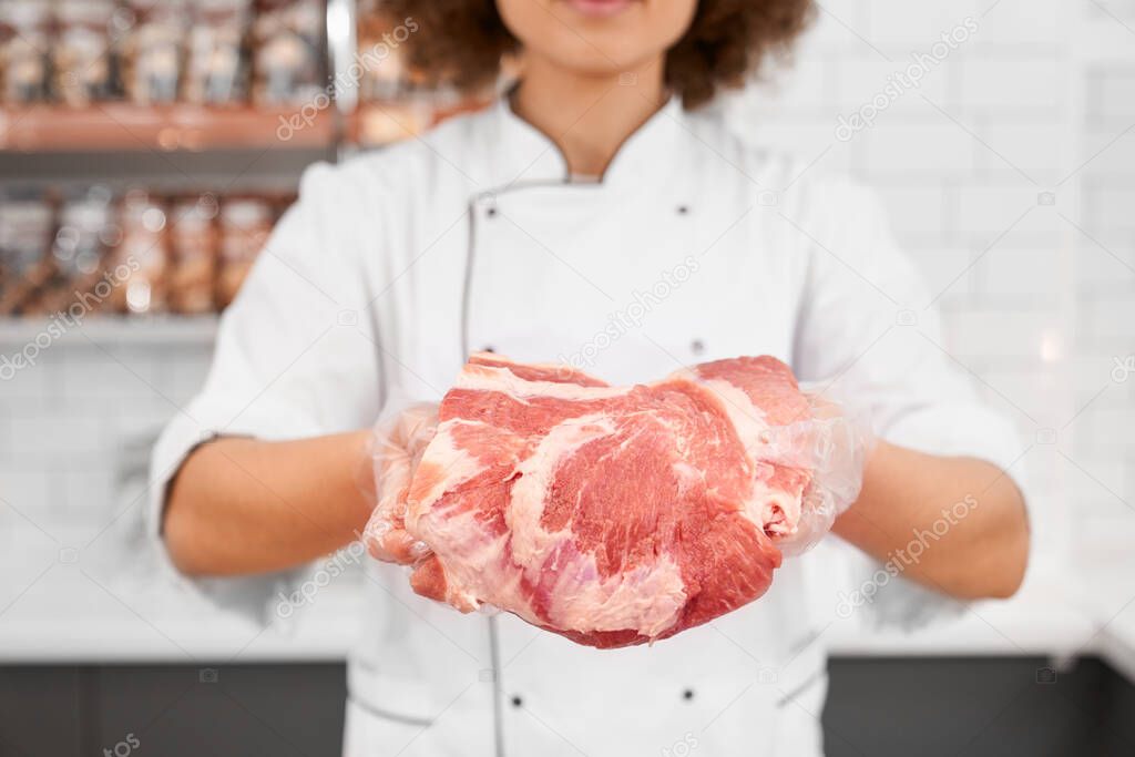 Incognito female butcher showing meat in supermarket.