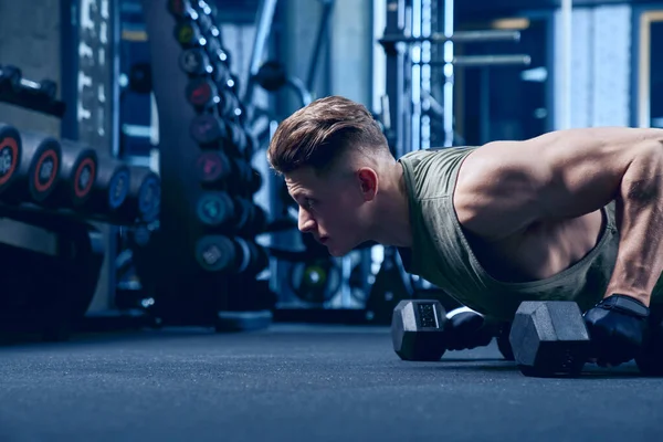 Bodybuilder doet push-ups met behulp van halters. — Stockfoto