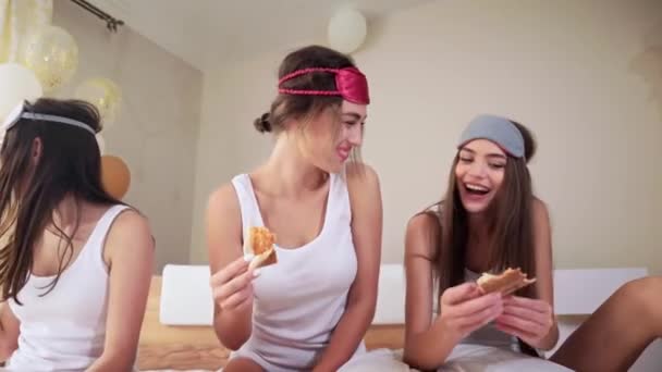 Chicas elegantes sentadas en la cama y comiendo pizza . — Vídeos de Stock