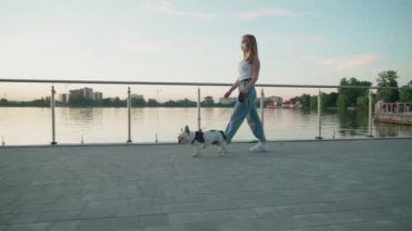 Yüz maskesi takan genç bir kadın köpekle yürüyor..